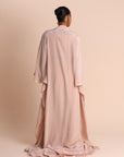 Person wearing a long, light pink Abaya against a beige background