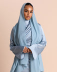 Woman wearing a light blue hijab and outfit against a beige background