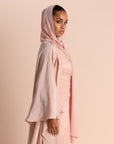 Woman wearing a light pink hijab and abaya against a beige background