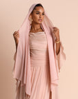 Woman wearing a light pink dress with a matching headscarf against a beige background
