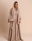 Woman wearing a beige abaya with a matching Hijab on a beige background