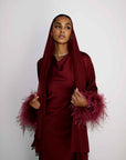 Woman wearing a burgundy outfit with feathered sleeves against a white background