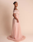 Woman wearing a pink off-shoulder gown with feathered hem on a beige background