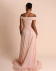 Woman wearing a pink off-shoulder gown with feathered hem on a beige background