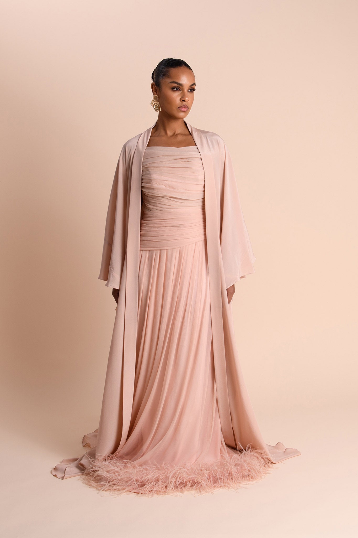Woman wearing a long, flowing pink dress with a matching Abaya against a beige background