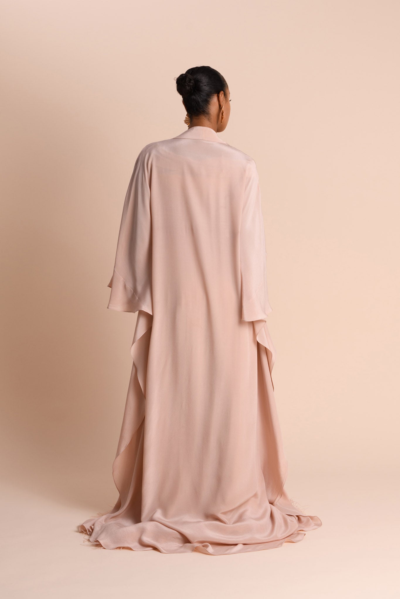 Person wearing a long, light pink Abaya against a beige background