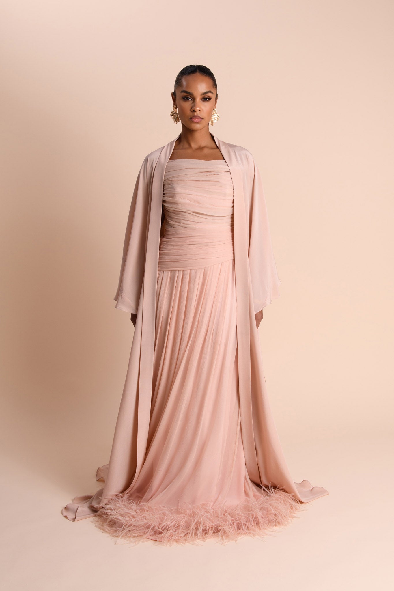 Woman wearing a pink dress with a matching abaya against a beige background