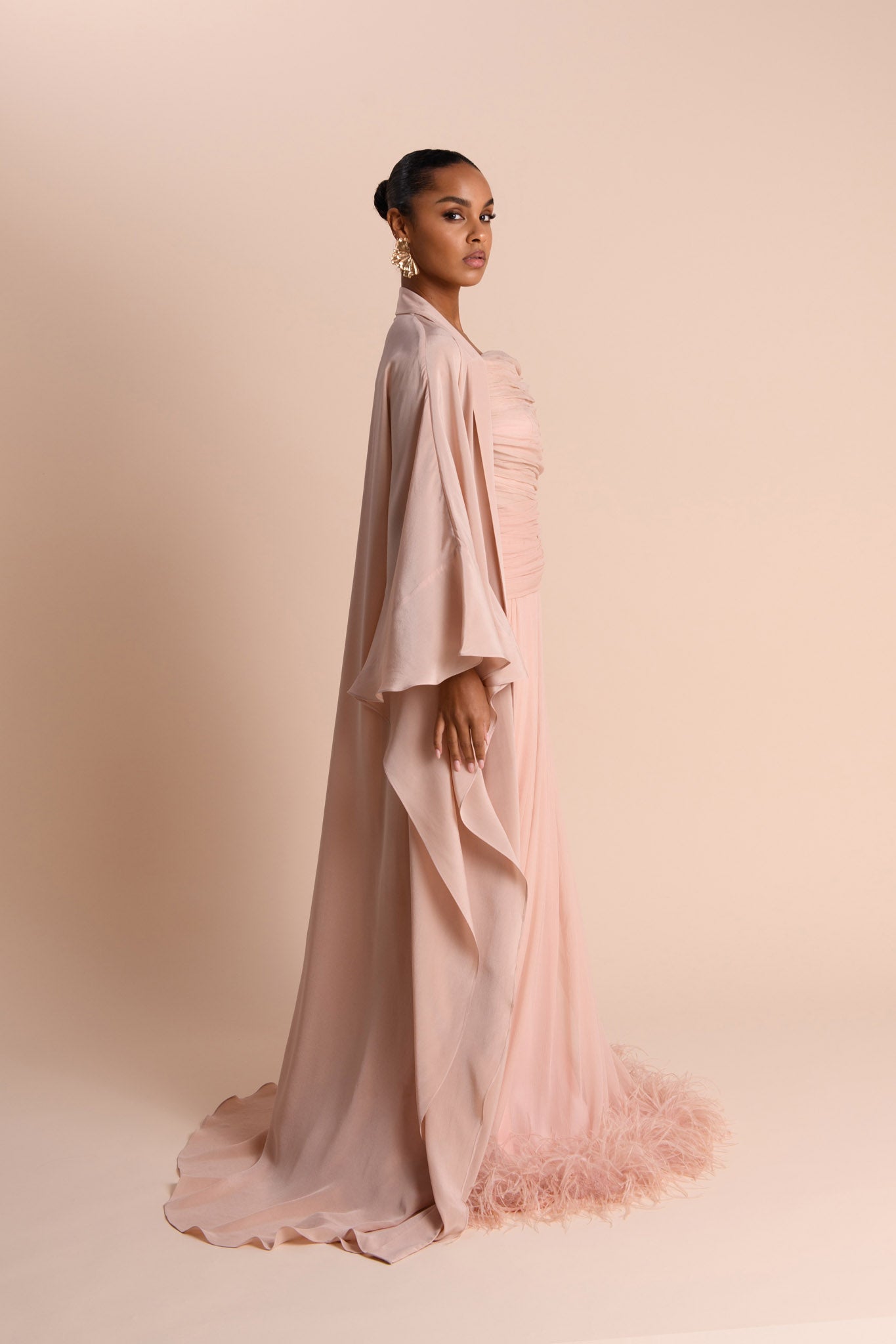 Woman wearing a light pink dress with an abaya against a beige background