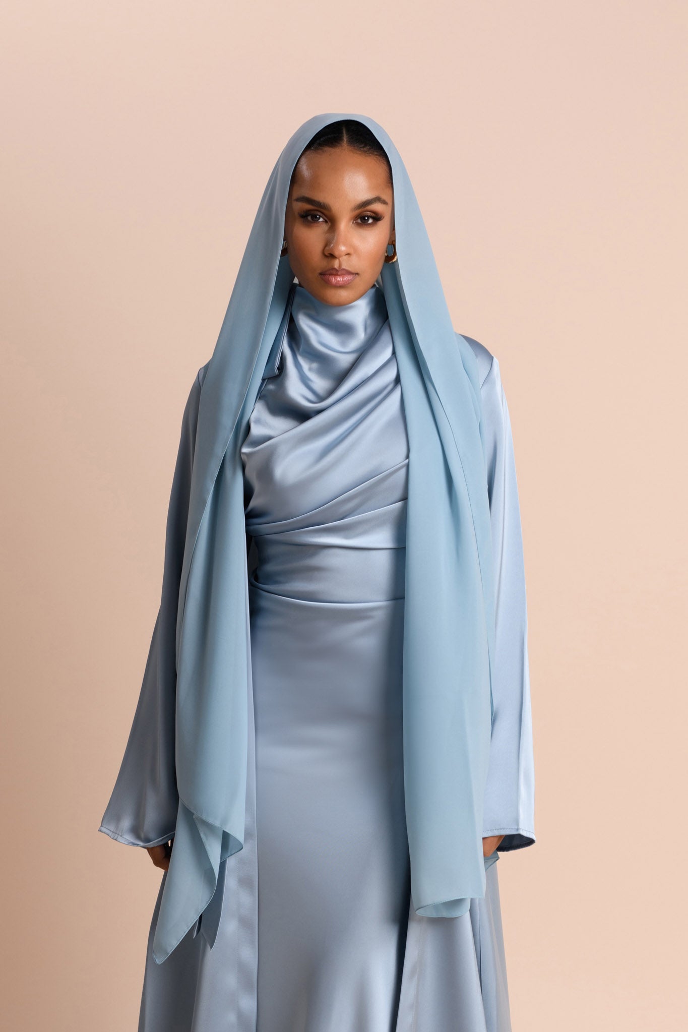 Woman wearing a light blue abaya against a beige background