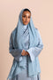 Woman wearing a light blue hijab and outfit against a beige background