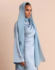 Woman wearing a light blue hijab and dress against a beige background