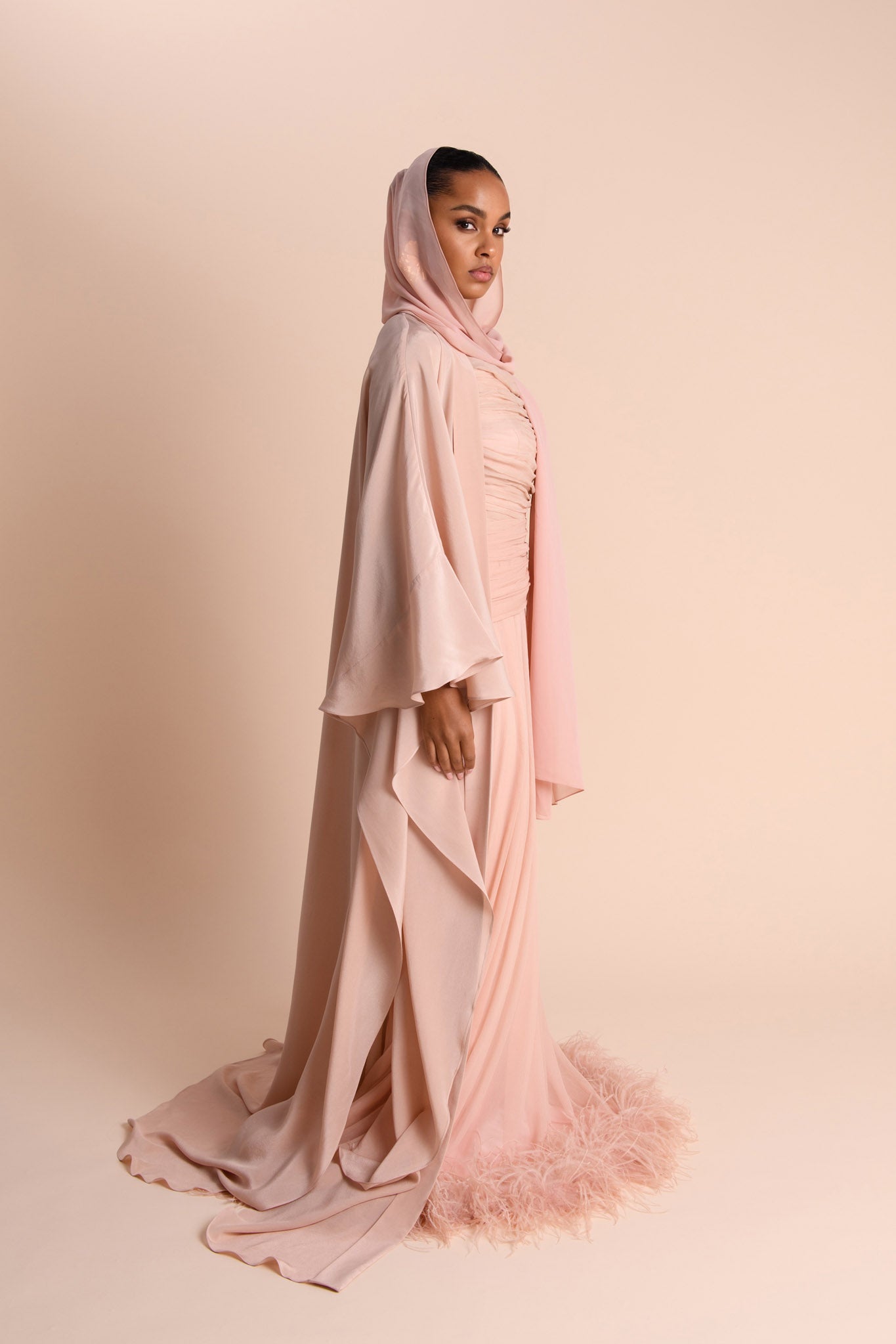 Woman wearing a pink hijab and dress against a beige background