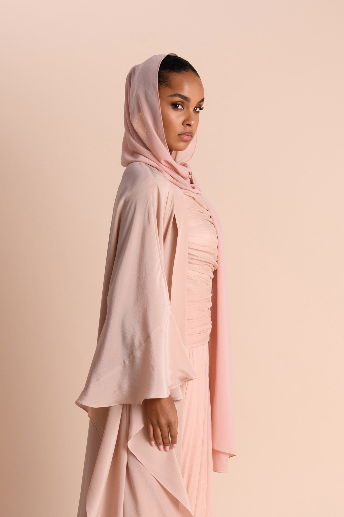 Woman wearing a light pink hijab and abaya against a beige background