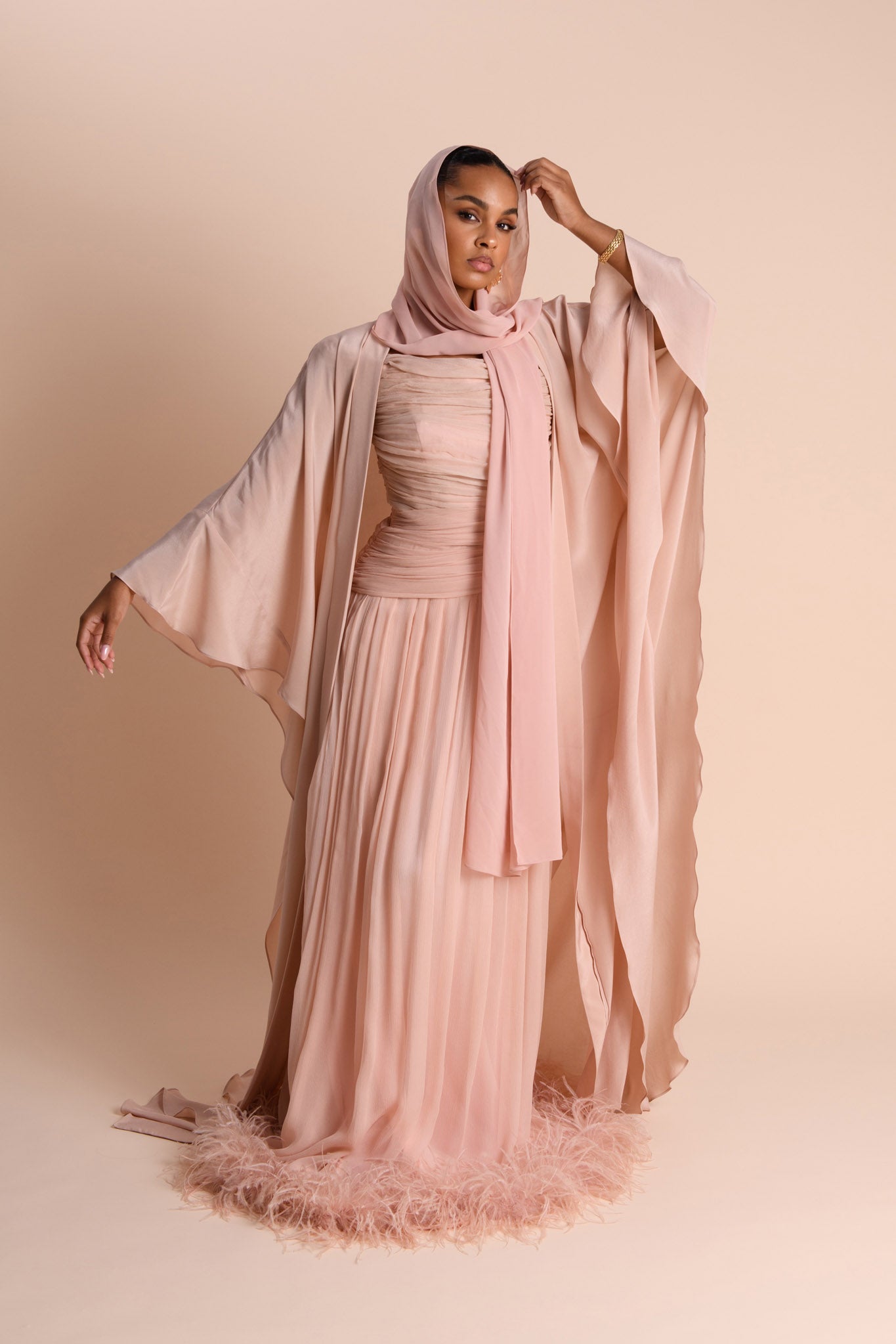 Woman wearing a flowing pink dress and hijab against a beige background