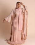 Woman wearing a flowing pink dress and hijab against a beige background