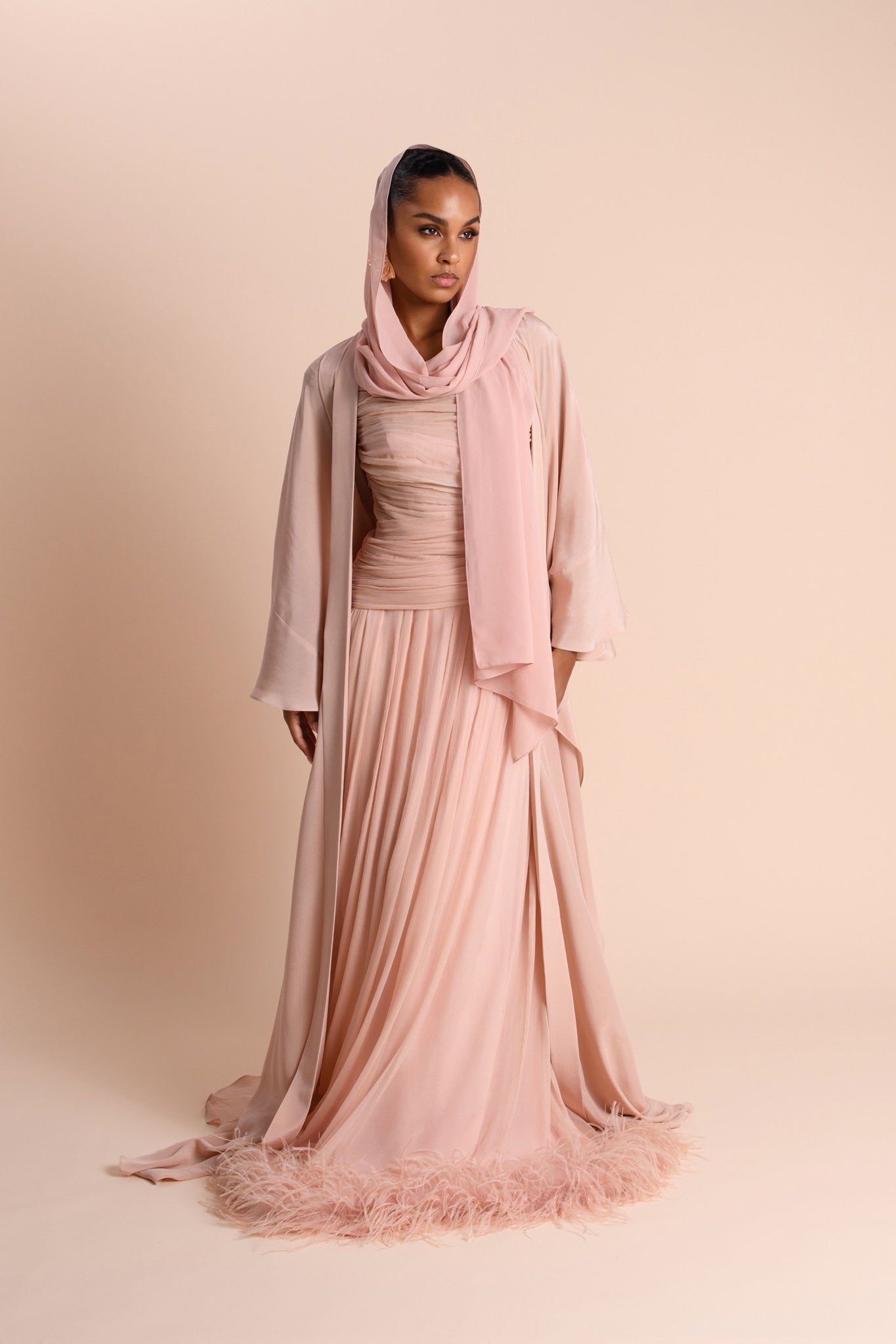 Woman wearing a pink hijab and dress against a beige background