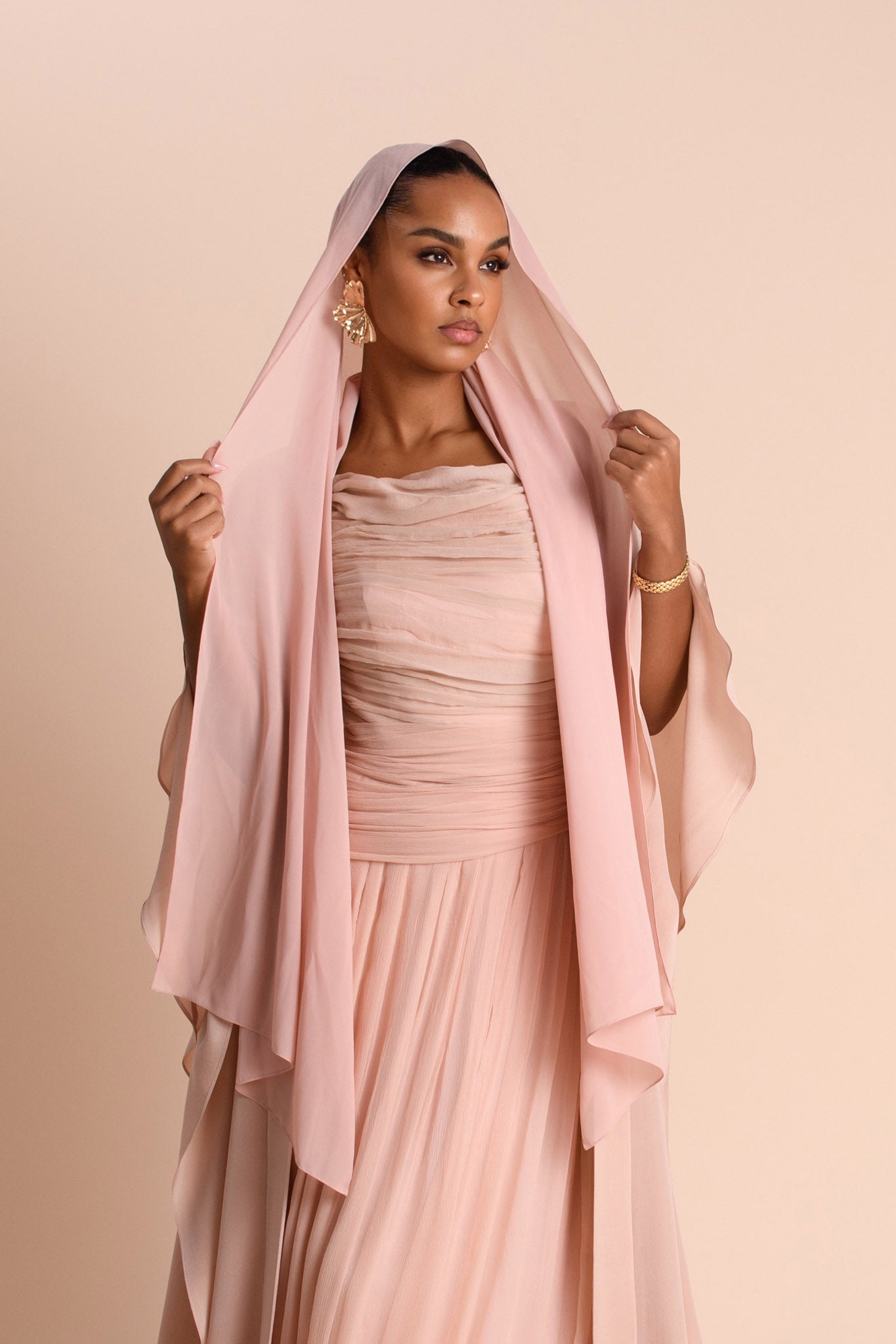 Woman wearing a light pink dress with a matching headscarf against a beige background