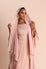 Woman wearing a light pink dress with a matching headscarf against a beige background