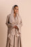 Woman wearing a beige hijab and dress against a beige background