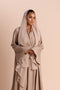 Woman wearing a beige hijab and dress against a beige background