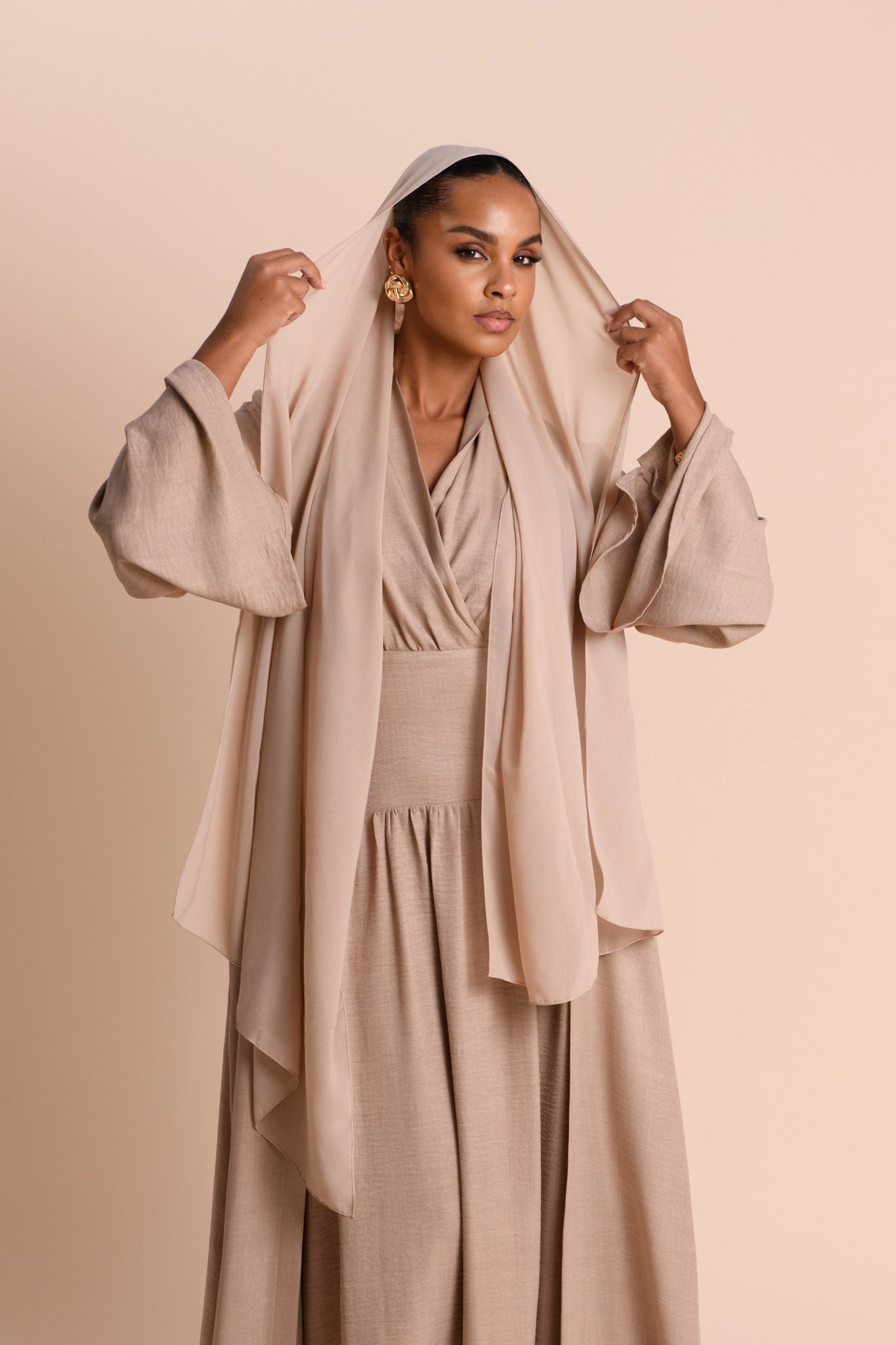 Woman wearing a beige outfit with a matching Hijab against a beige background