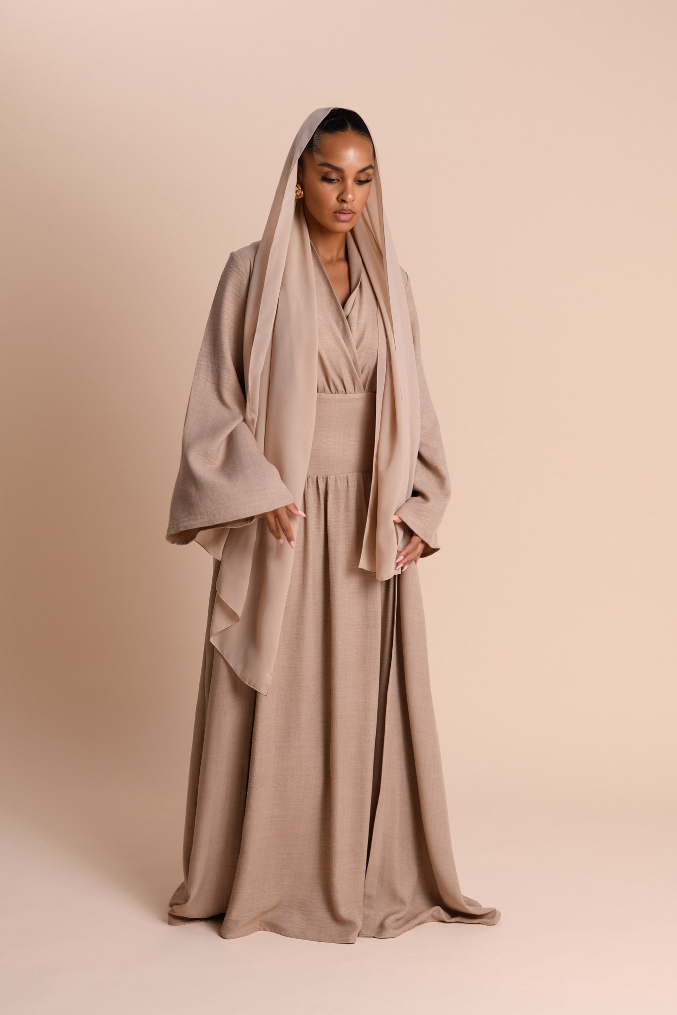 Woman wearing a beige abaya with a matching Hijab on a beige background