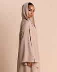 Woman wearing a beige hijab and dress against a beige background