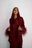 Woman wearing a burgundy outfit with feathered sleeves against a white background