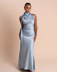 Woman wearing a light blue gown with a draped neckline against a beige background