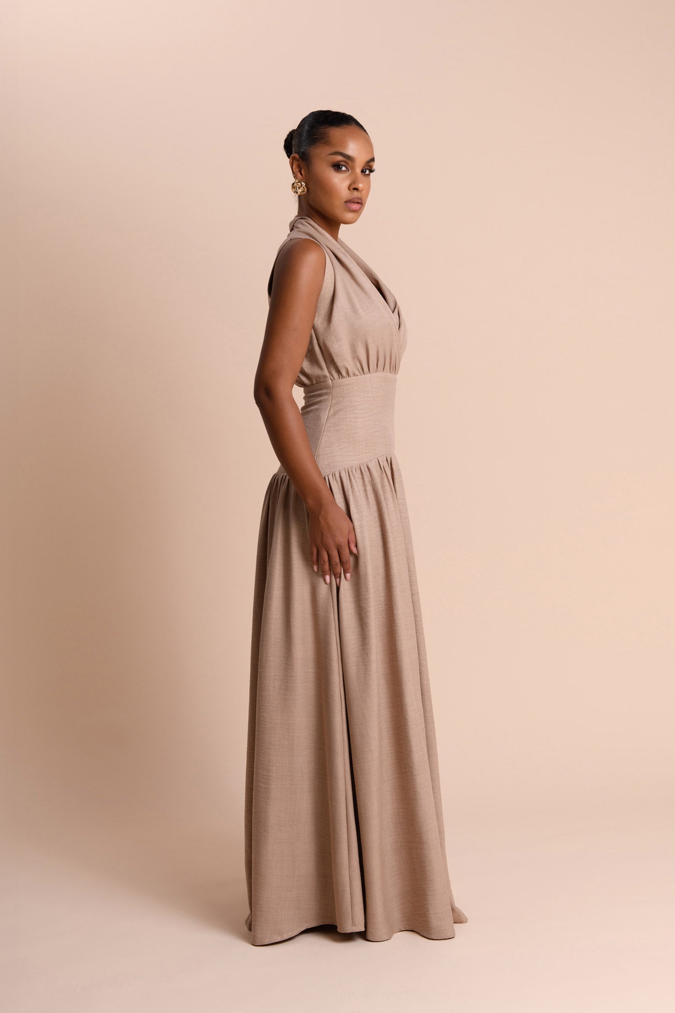 Woman wearing a beige halter neck gown against a beige background