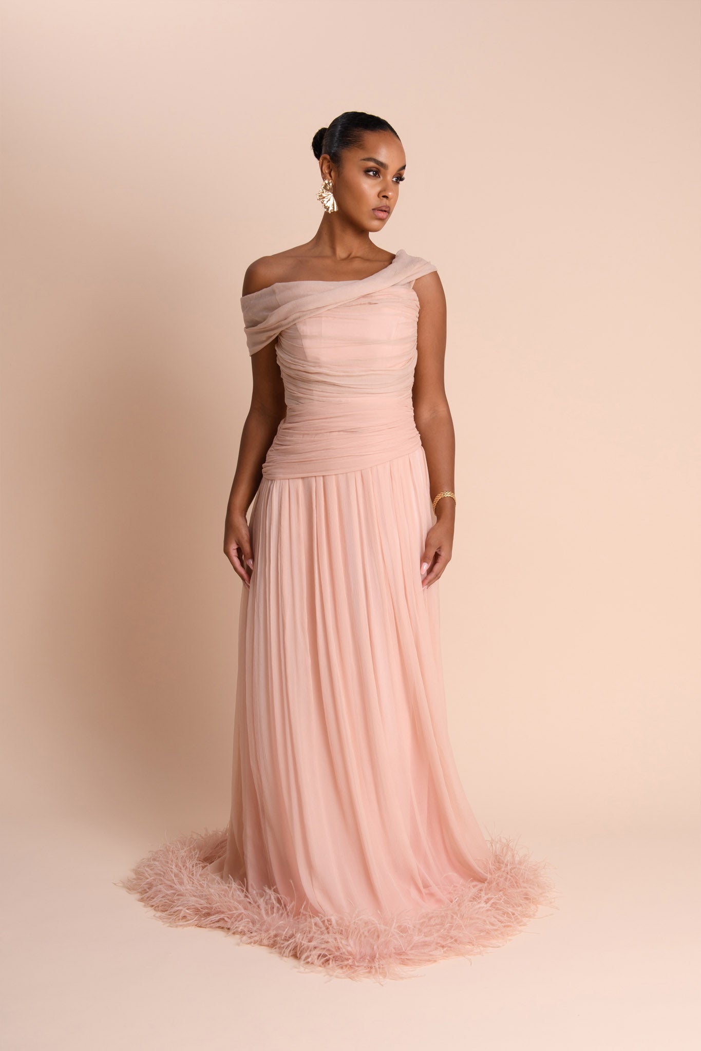 Woman wearing a one-shoulder pink gown with feathered skirt on a beige background