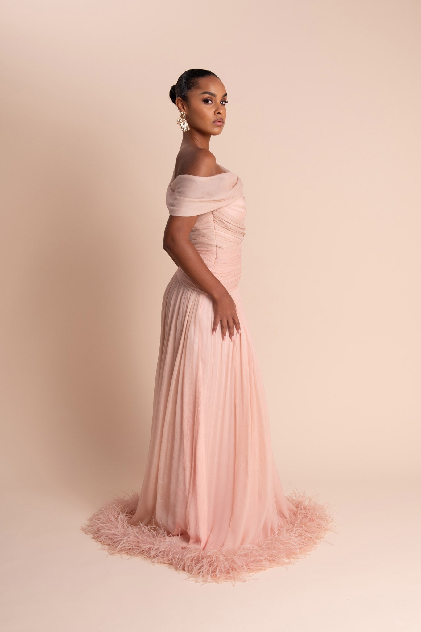 Woman wearing a pink off-shoulder gown with feathered hem on a beige background