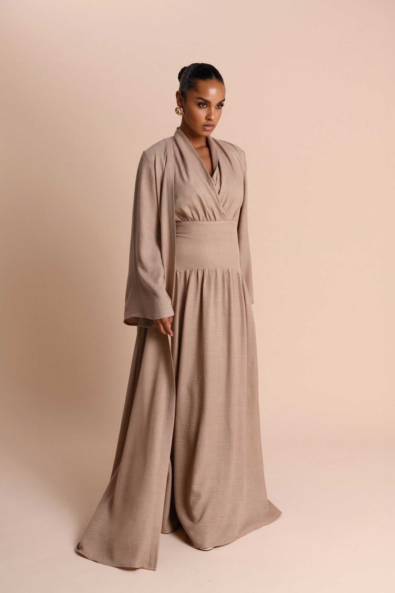 Woman wearing a long, light brown dress against a beige background