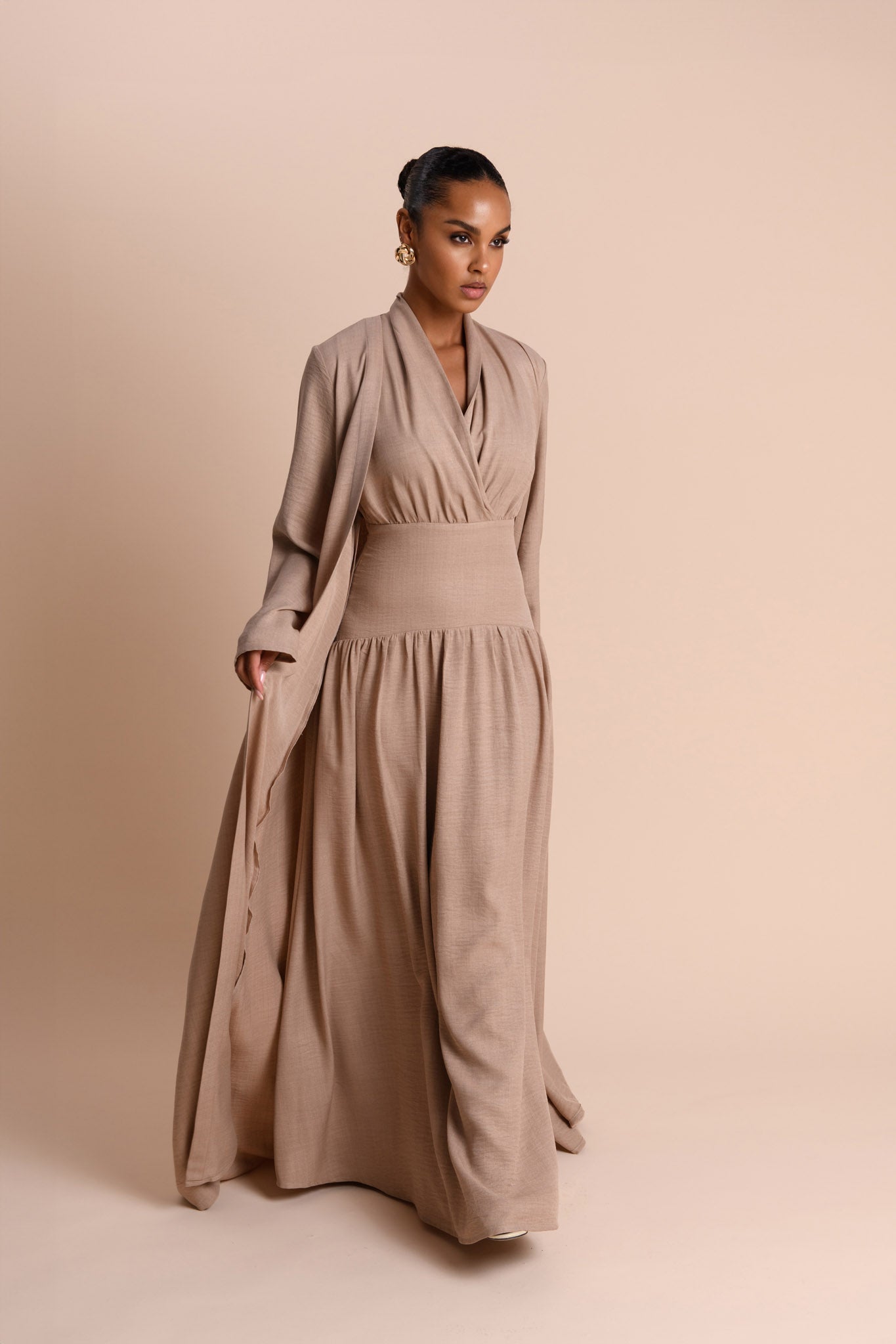 Woman wearing a long beige dress against a beige background