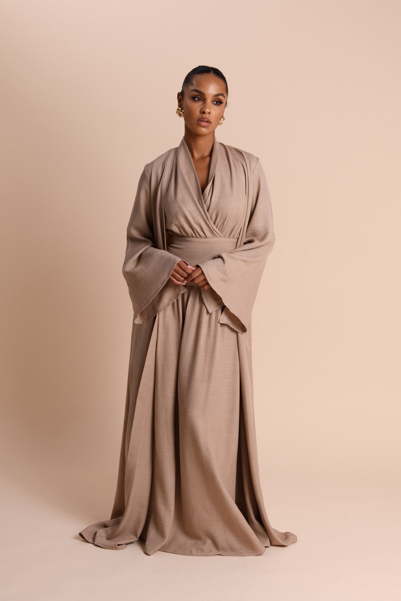 Woman wearing a long, flowing beige dress against a beige background