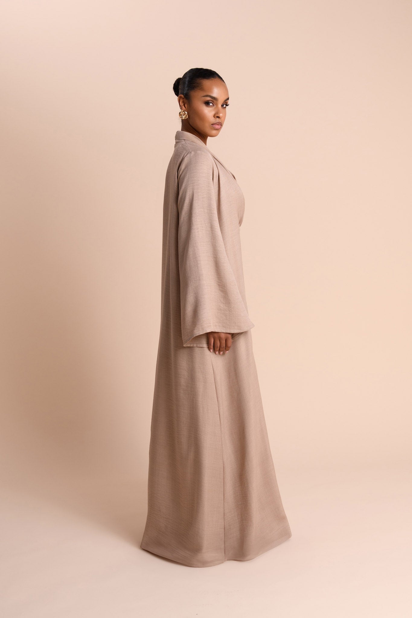 Woman wearing a long beige coat against a beige background