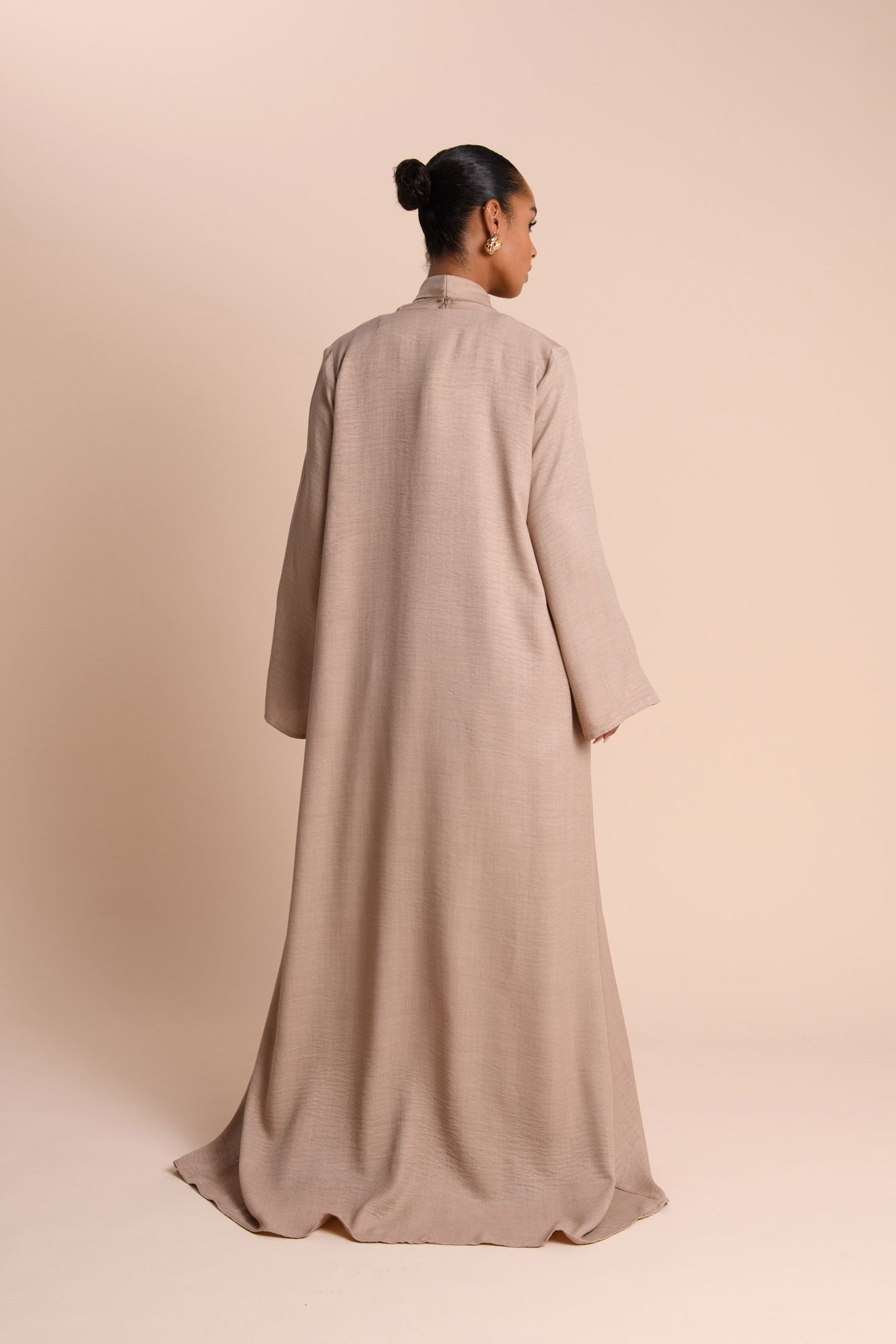 Woman wearing a long beige dress against a beige background